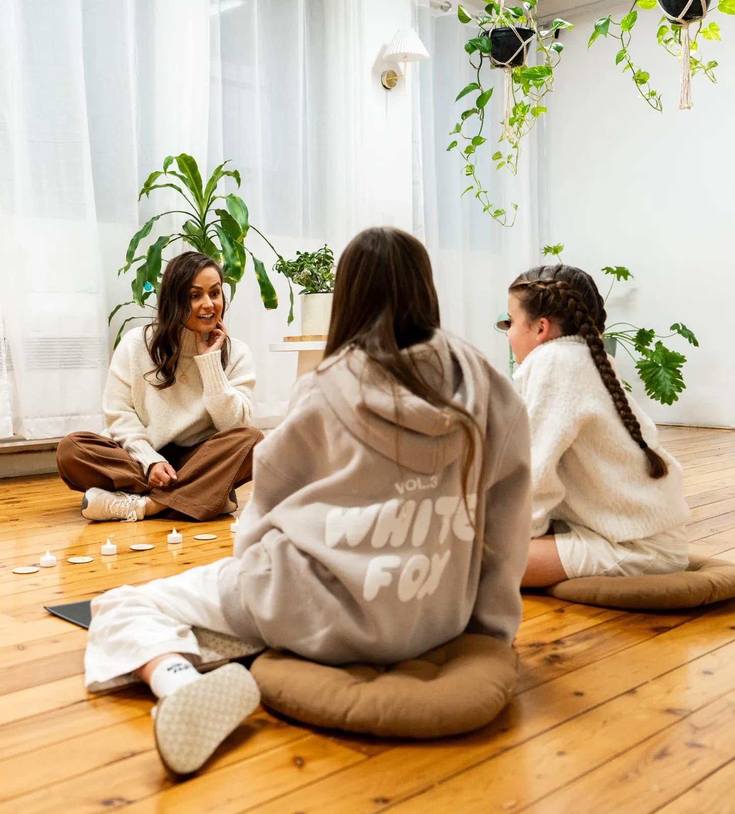 Ellie sitting in a circle on floor cushions with two teenage girls during a group program
